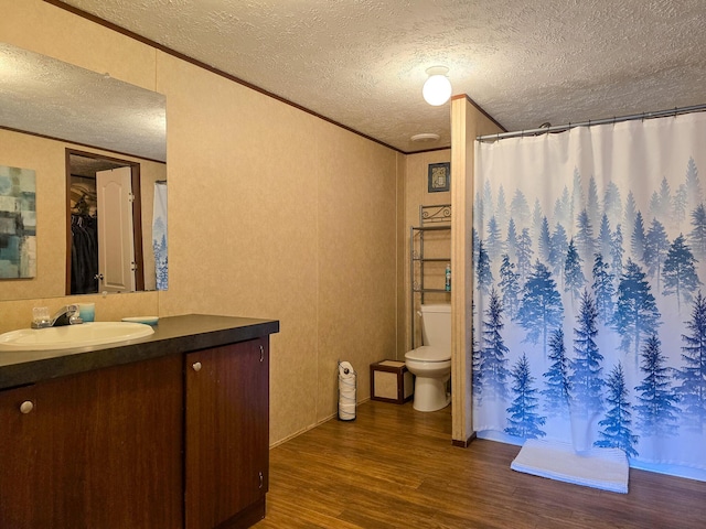 bathroom featuring a textured ceiling, toilet, wood finished floors, vanity, and crown molding