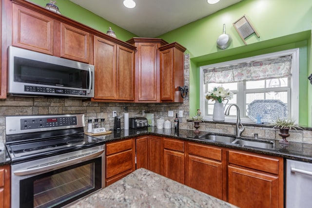 kitchen with appliances with stainless steel finishes, backsplash, dark stone countertops, and a sink