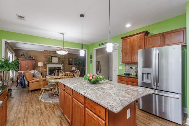 kitchen with a stone fireplace, visible vents, light wood-type flooring, decorative backsplash, and stainless steel fridge