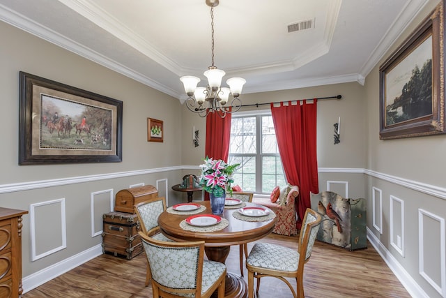 dining area featuring a tray ceiling, visible vents, an inviting chandelier, ornamental molding, and wood finished floors