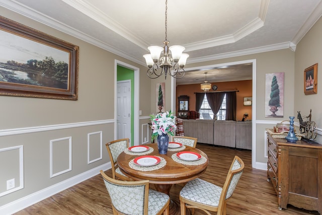 dining area featuring a notable chandelier, a raised ceiling, and wood finished floors