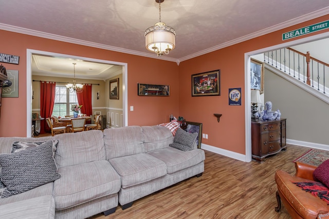 living area featuring crown molding, wood finished floors, a chandelier, baseboards, and stairs