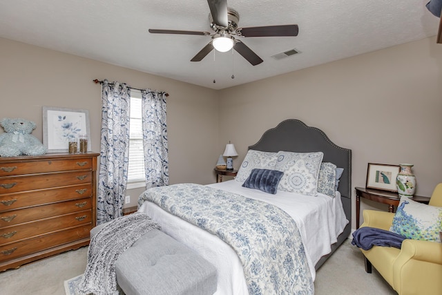 bedroom featuring a ceiling fan, visible vents, light carpet, and a textured ceiling