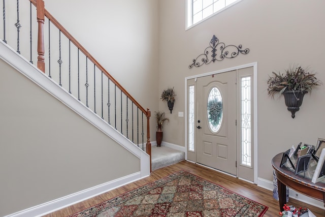 entrance foyer featuring stairway, wood finished floors, a towering ceiling, and a healthy amount of sunlight