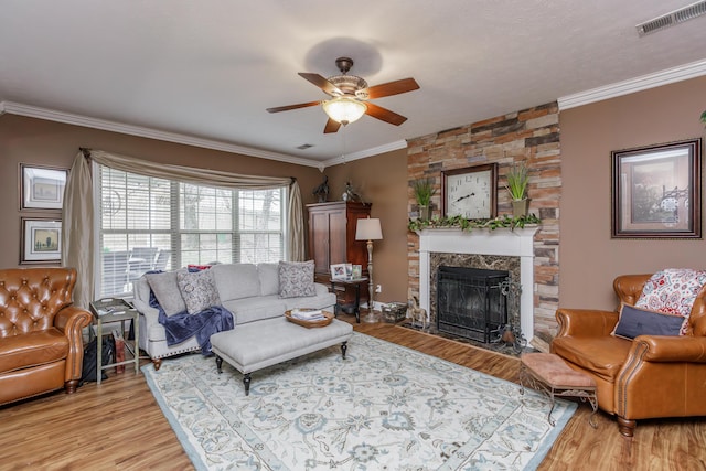 living room featuring a stone fireplace, visible vents, crown molding, and light wood-style flooring