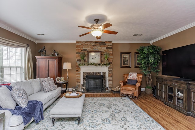 living area featuring a stone fireplace, ornamental molding, wood finished floors, and visible vents