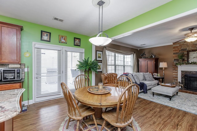 dining area with visible vents, a ceiling fan, ornamental molding, wood finished floors, and a fireplace