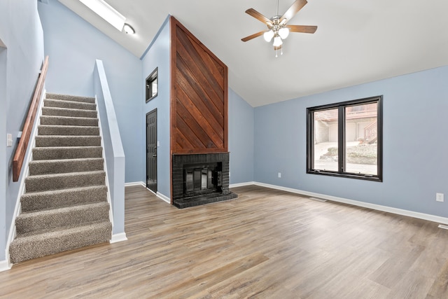 unfurnished living room with stairs, a brick fireplace, baseboards, and light wood-style floors