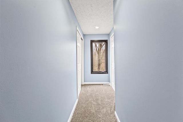 hallway featuring carpet flooring, a textured ceiling, and baseboards