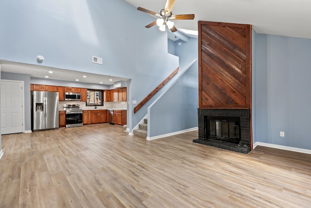 unfurnished living room with visible vents, baseboards, stairway, light wood-type flooring, and a brick fireplace