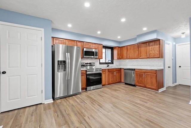 kitchen with decorative backsplash, brown cabinetry, light wood-style flooring, appliances with stainless steel finishes, and light countertops