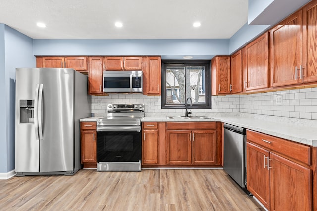 kitchen featuring brown cabinets, stainless steel appliances, light countertops, light wood-style floors, and a sink