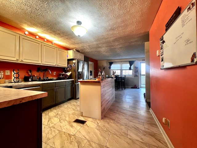 kitchen featuring a kitchen island with sink, a sink, visible vents, wooden counters, and stainless steel refrigerator with ice dispenser