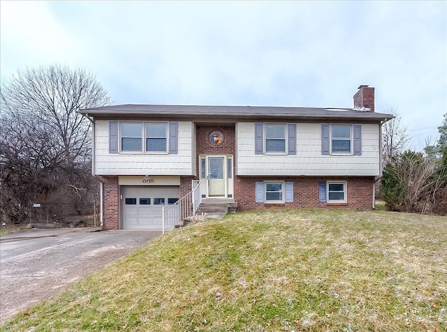 raised ranch featuring brick siding, a chimney, an attached garage, driveway, and a front lawn