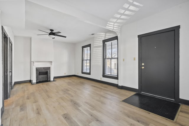 unfurnished living room featuring light wood finished floors, a premium fireplace, visible vents, and baseboards