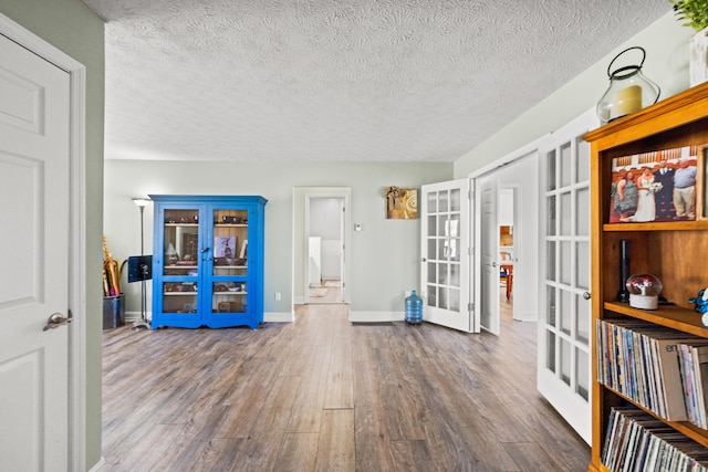 interior space featuring a textured ceiling, french doors, wood finished floors, and baseboards