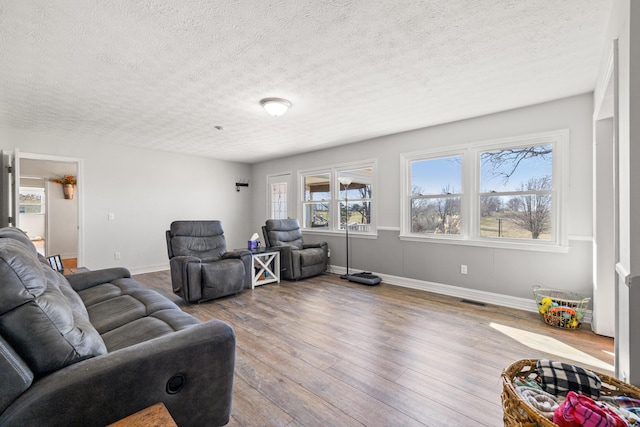 living area featuring plenty of natural light, visible vents, baseboards, and wood finished floors