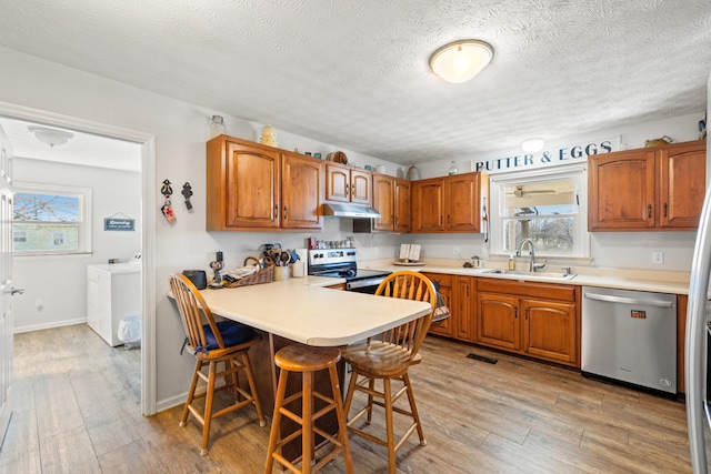 kitchen with light wood-style flooring, under cabinet range hood, stainless steel appliances, separate washer and dryer, and a sink