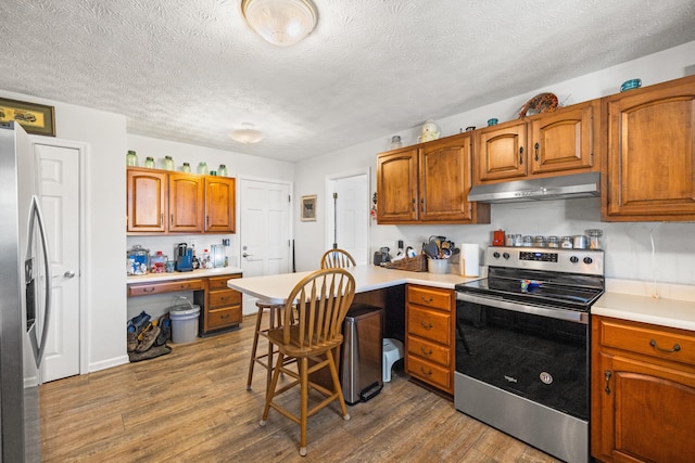 kitchen with dark wood finished floors, light countertops, appliances with stainless steel finishes, built in study area, and under cabinet range hood