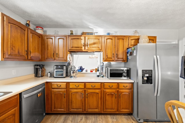 kitchen featuring light wood-type flooring, brown cabinetry, appliances with stainless steel finishes, and light countertops