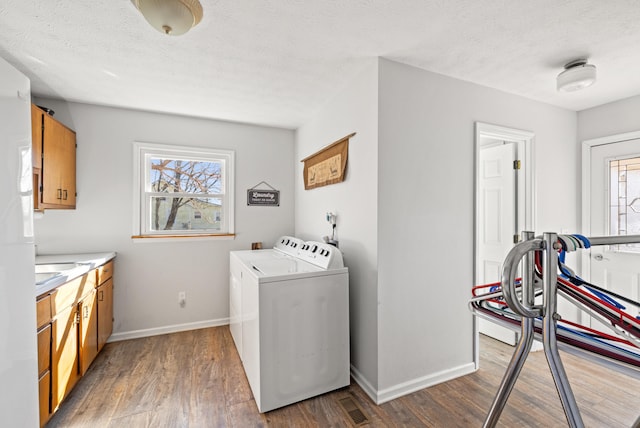 washroom featuring a healthy amount of sunlight, cabinet space, washer and clothes dryer, and wood finished floors