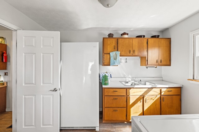 kitchen with brown cabinets, light countertops, a sink, and freestanding refrigerator