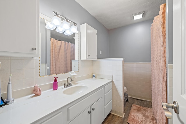 bathroom featuring toilet, wood finished floors, a textured ceiling, vanity, and tile walls