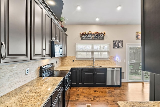 kitchen with a sink, backsplash, dark wood-style floors, appliances with stainless steel finishes, and light stone countertops