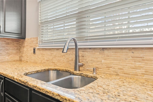 room details with a sink, light stone counters, tasteful backsplash, and dark cabinets