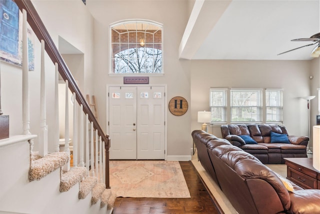 entrance foyer with a ceiling fan, wood finished floors, baseboards, a towering ceiling, and stairs