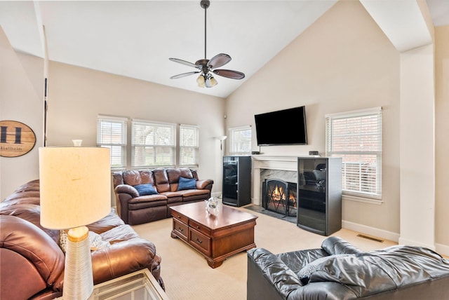 living area featuring a ceiling fan, visible vents, high vaulted ceiling, a fireplace, and light carpet