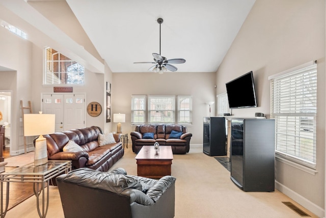 living room with baseboards, visible vents, high vaulted ceiling, ceiling fan, and light carpet