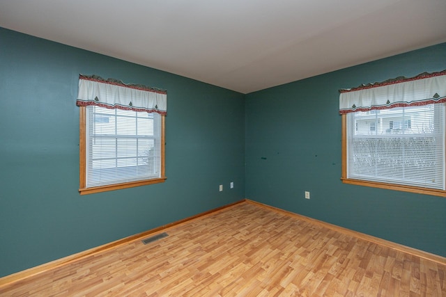 spare room featuring baseboards, visible vents, and wood finished floors