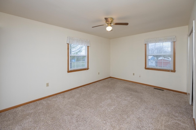 empty room with carpet flooring, ceiling fan, visible vents, and baseboards