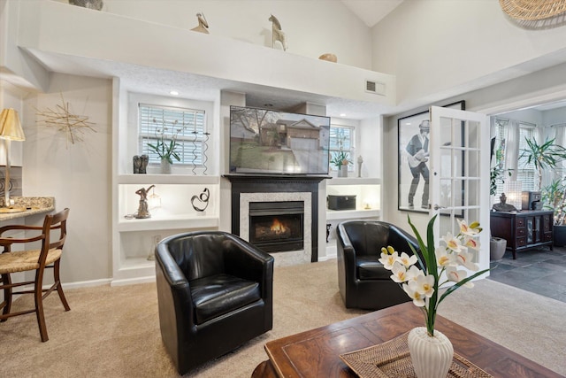 carpeted living room with visible vents, baseboards, a high ceiling, and a warm lit fireplace