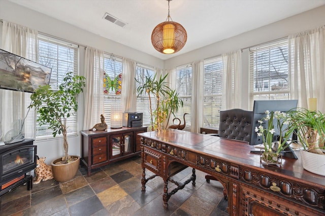 home office featuring visible vents, stone tile floors, and a wood stove