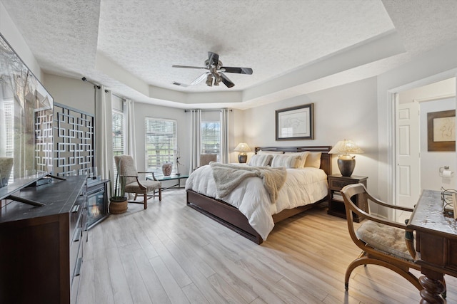 bedroom with visible vents, a ceiling fan, a textured ceiling, light wood-style floors, and a raised ceiling