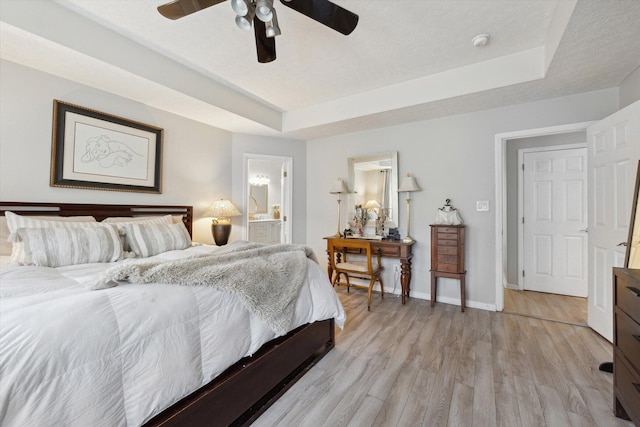 bedroom featuring baseboards, ceiling fan, light wood-style floors, a raised ceiling, and connected bathroom