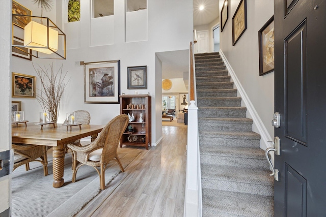 interior space with light wood-type flooring, baseboards, a towering ceiling, and stairs