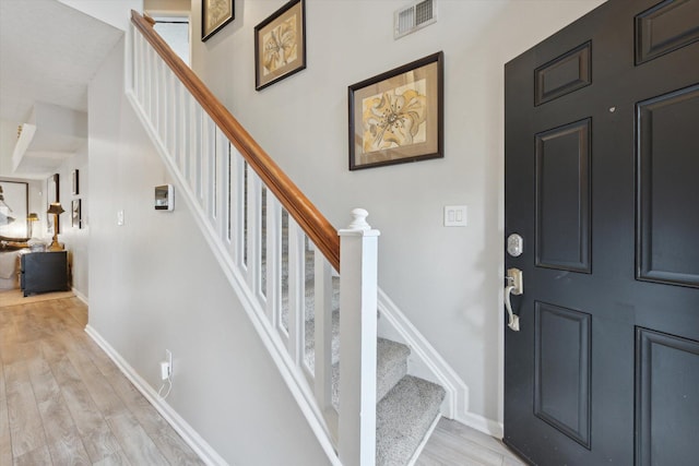 foyer entrance featuring light wood finished floors, visible vents, stairs, and baseboards