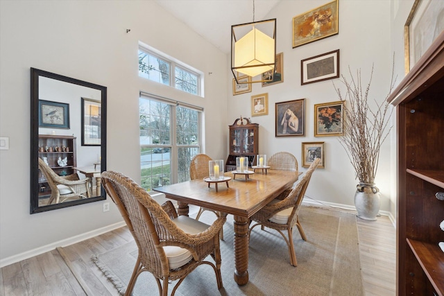 dining room with light wood-style floors, baseboards, and a towering ceiling