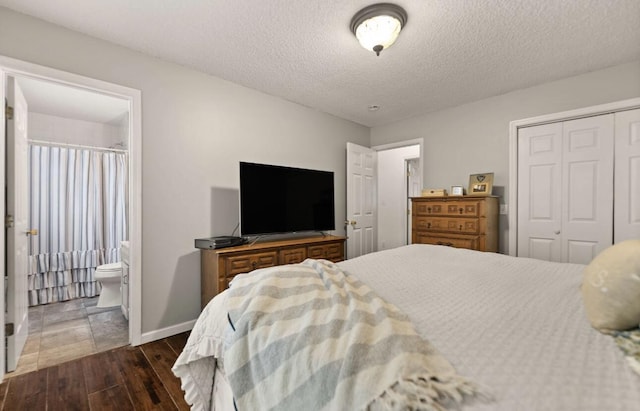 bedroom with a textured ceiling, dark wood-style flooring, baseboards, a closet, and ensuite bath