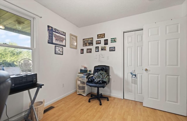 office with visible vents, light wood-style flooring, baseboards, and a textured ceiling