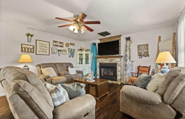 living area with dark wood-style flooring, ceiling fan, a stone fireplace, and a textured ceiling