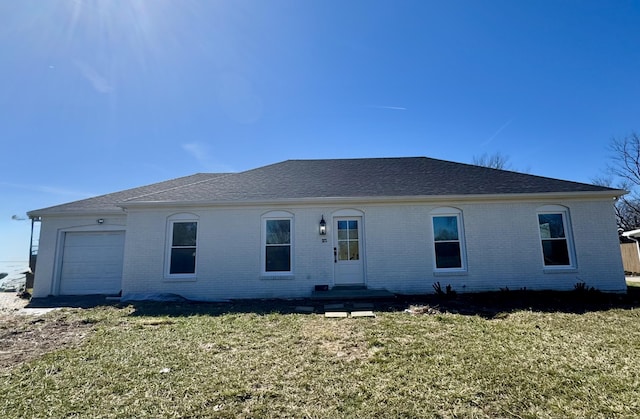 rear view of property with a garage, roof with shingles, a lawn, and brick siding