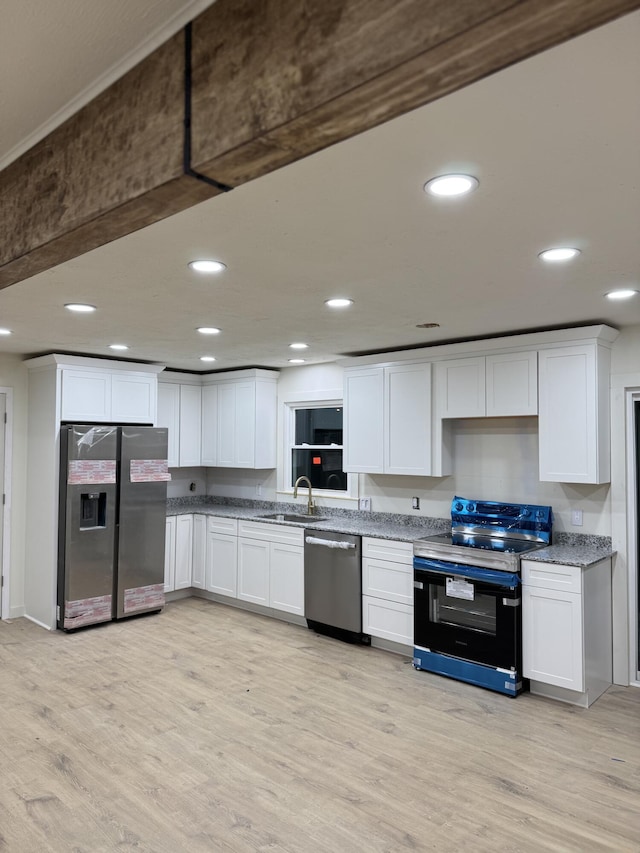 kitchen with appliances with stainless steel finishes, light wood-type flooring, white cabinetry, and a sink