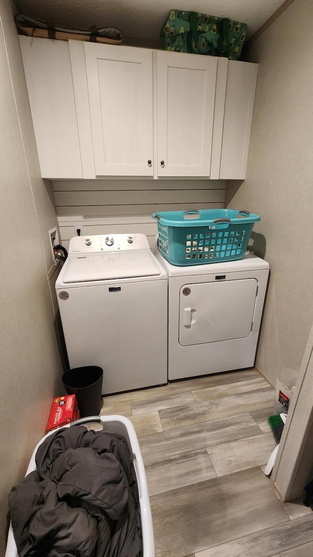 laundry area featuring light wood finished floors, separate washer and dryer, and cabinet space