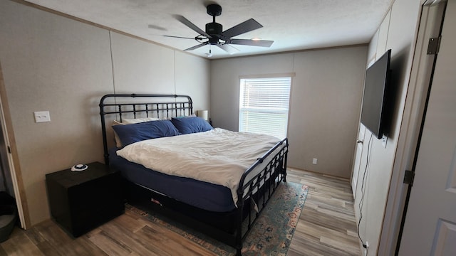 bedroom with ceiling fan, a textured ceiling, light wood-type flooring, and crown molding