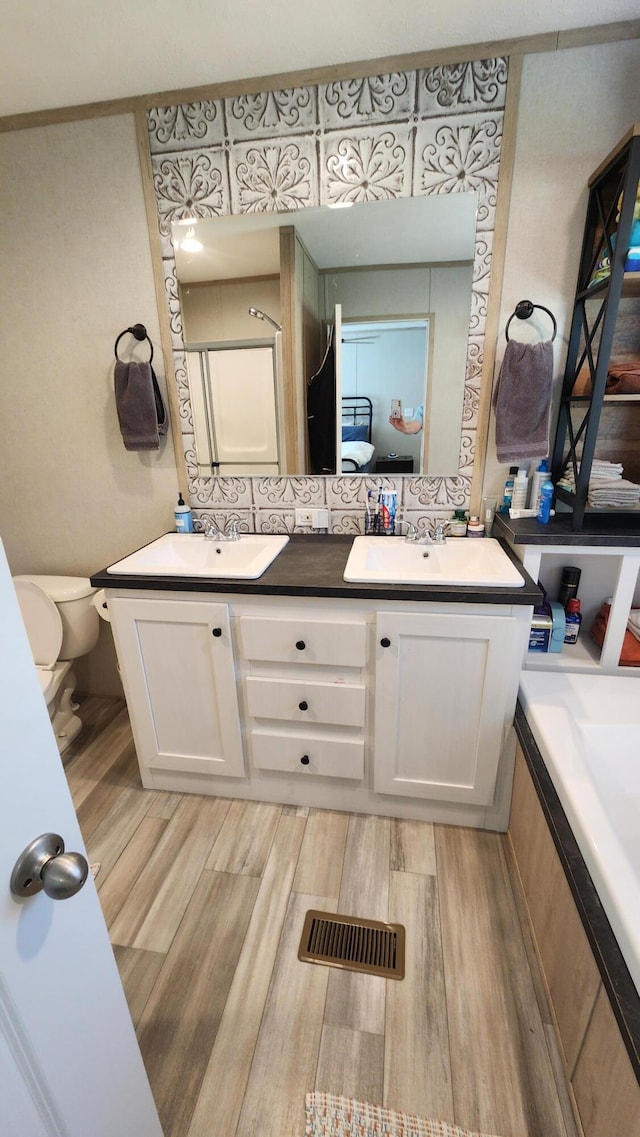 bathroom featuring toilet, wood finished floors, a sink, visible vents, and double vanity