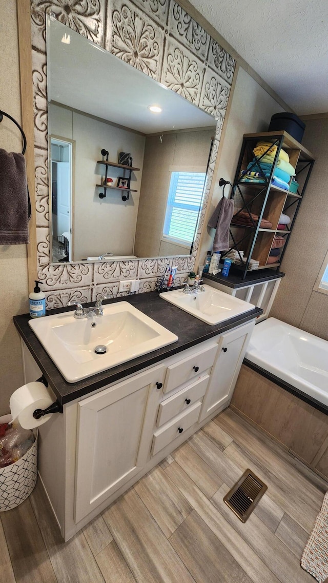 full bathroom with double vanity, visible vents, a sink, and wood finished floors